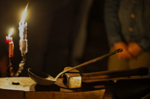 Un cazo de hierro sobre el martillo de los ferrreiros, iluminados por velas.